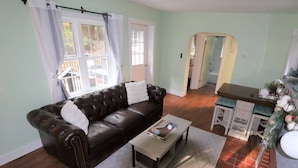 A living room with a dark brown leather sofa, a light-colored coffee table, and a kitchen area with a white countertop and a Christmas tree. - Romantic Waterfront Cottage for Cherry Springs (Coudersport)