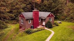 A house with a red chimney, surrounded by a lush green lawn and dense forest. - Romantic Waterfront Cottage for Cherry Springs (Coudersport)