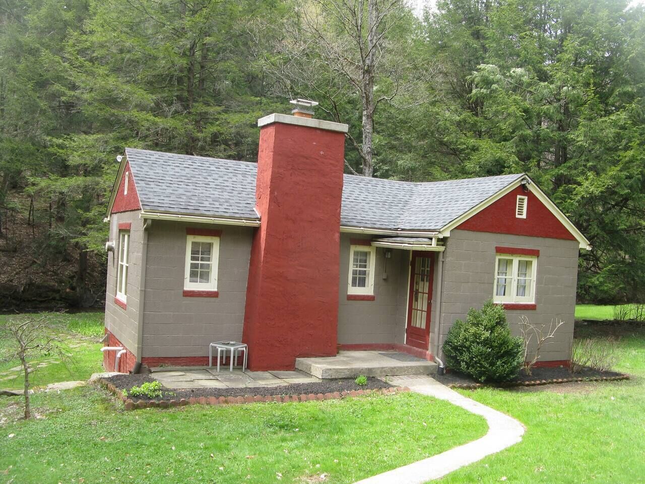 Una casa de dos pisos con una chimenea roja, un porche pequeño y un sendero que conduce a la entrada.