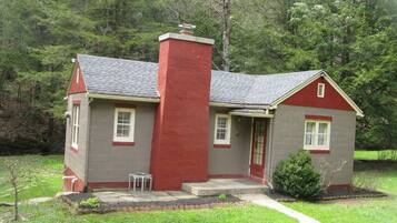 Una casa de dos pisos con una chimenea roja, un porche pequeño y un sendero que conduce a la entrada.