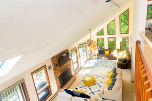 A spacious living room with a fireplace, large windows, and a high ceiling. - Lakefront- Hot Tub/Foosball table/Pool table/Kayak (Long Pond)