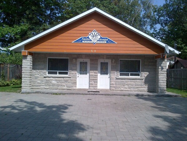 A two-story building with a stone facade, a wooden gable roof, and a sign for 'Suites of Vasaga Weekly Rentals'. - Beach Area 1 Suites Of Wasaga (Wasaga Beach)