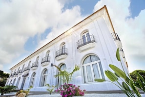 A white building with arched windows and balconies, surrounded by small plants and a clear sky. - Albaida Nature (Moguer)