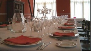 Un comedor con varias mesas dispuestas para una comida, cada una con platos, cubiertos y copas de vino.