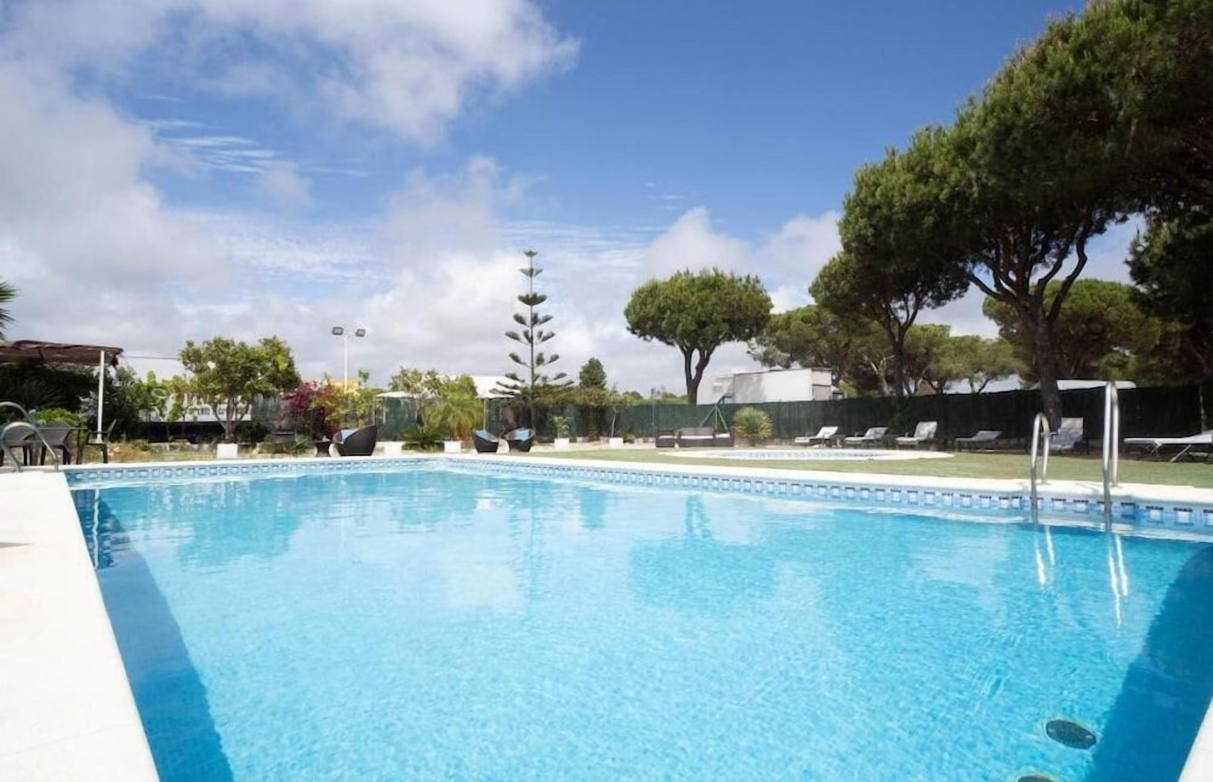 A swimming pool with lounge chairs and a tall tree in the background.