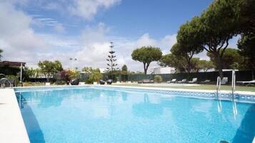A swimming pool with lounge chairs and a tall tree in the background.
