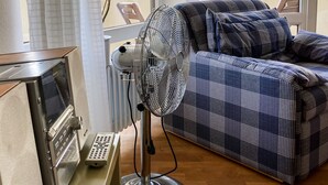Una habitación con un sofá estampado, un ventilador de pie y un radiador.
