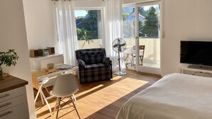 Un dormitorio con cama, escritorio y silla, televisión, ventilador y vista al exterior a través de una puerta corrediza.