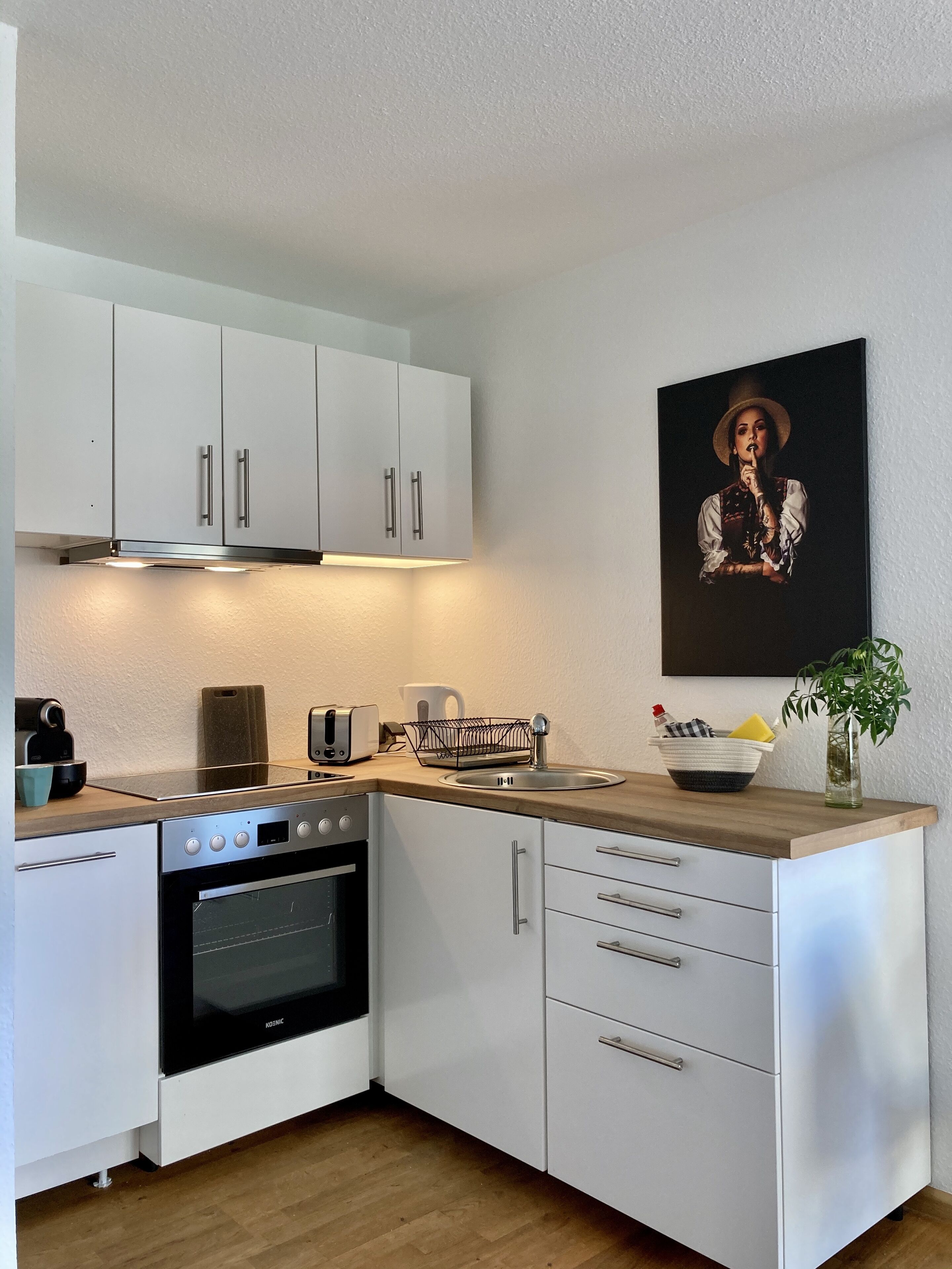 A modern kitchen with white cabinets, a built-in oven, a coffee maker, and a sink.
