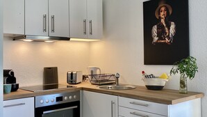Una cocina moderna con armarios blancos, horno empotrado, cafetera y pileta.