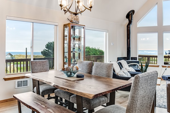 A dining area with a wooden table and chairs, a glass cabinet with decorative items, and a view of the ocean through large windows.