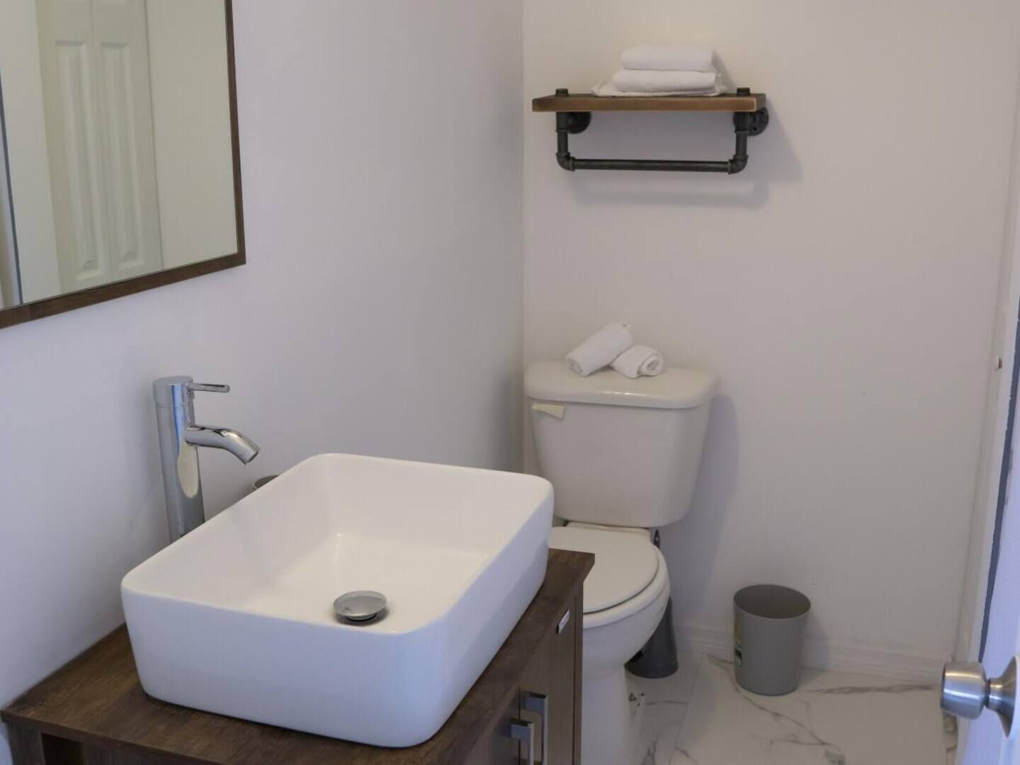 A bathroom with a white sink, toilet, and a small trash bin.