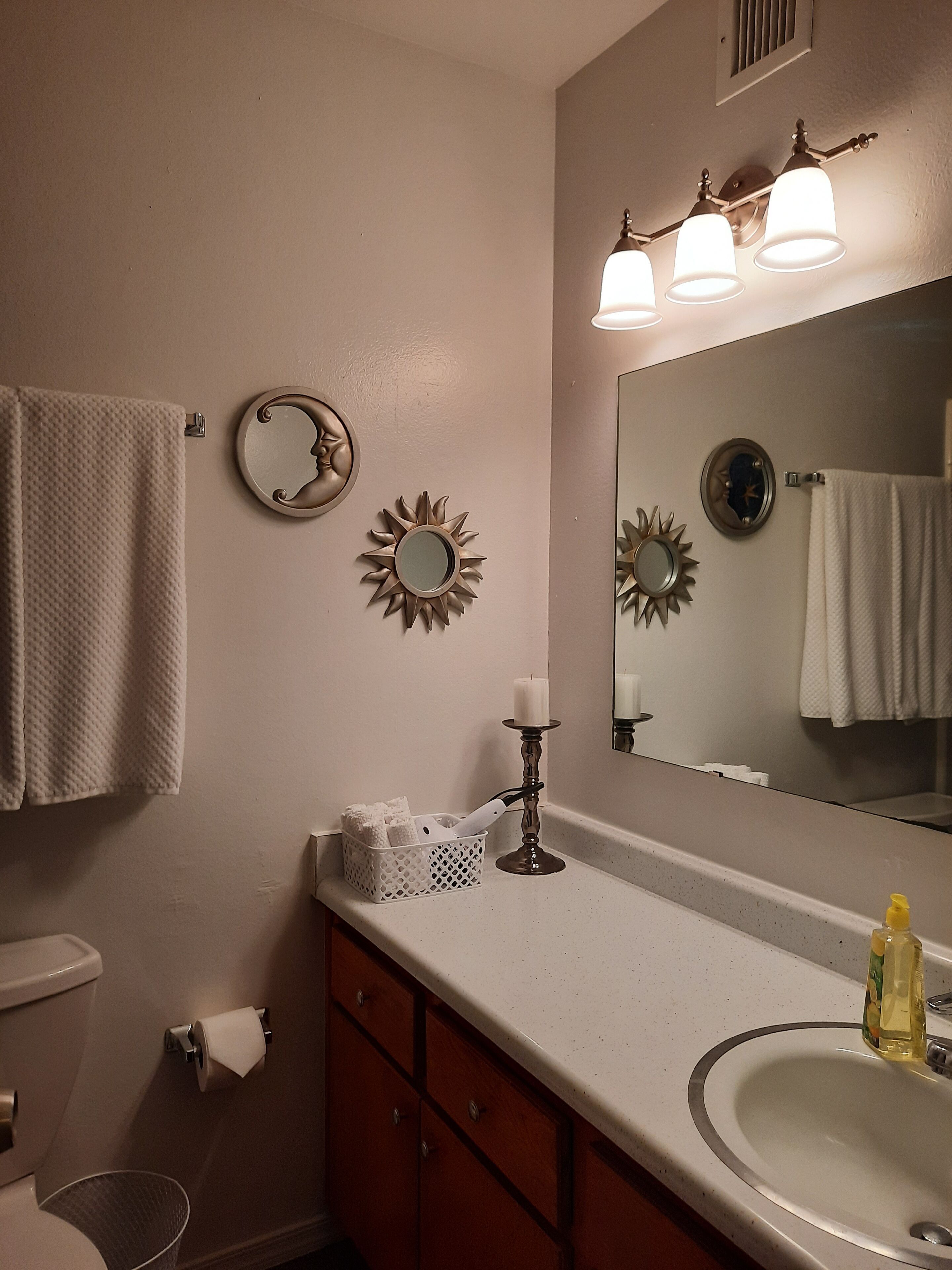 A bathroom with a sink, mirror, towel rack, decorative wall mirrors, and a candle.