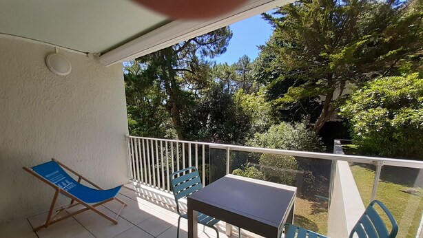 Un balcon avec une table et deux chaises, une balustrade blanche et une vue sur les arbres et la verdure.