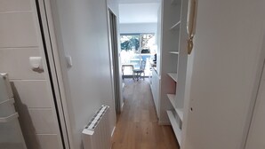 Un couloir étroit doté d’un plancher en bois, de murs blancs et d’une vue sur un coin repas avec une table et des chaises.