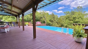Una terraza techada con piscina, sillas de madera y un granero rojo al fondo.