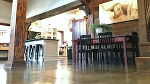 Un interior rústico con vigas de madera a la vista, una zona de bar con taburetes y un cuadro grande en la pared.