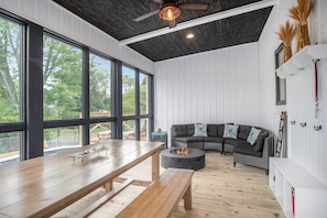 Relax in this spacious room with a long dining table, cozy sofa, and fire pit, surrounded by expansive views of the surrounding greenery.