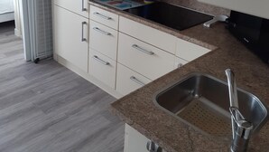 Una cocina con armarios blancos, encimera de granito, pileta de acero inoxidable y estufa integrada.