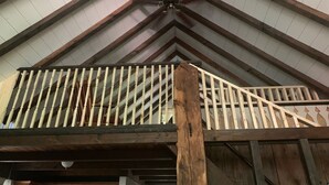 Un balcón de madera con barandilla, sostenido por un pilar central de madera.
