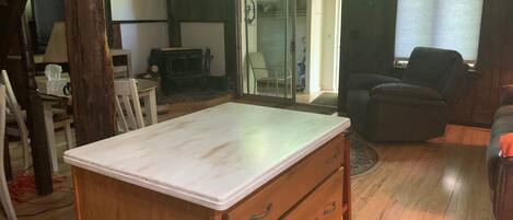 Una cocina de madera con encimera blanca y cajones, un comedor con sillas y una sala de estar con sofá y sillón.