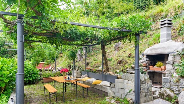 Un patio jardín con pérgola, asientos de piedra y un horno de piedra.