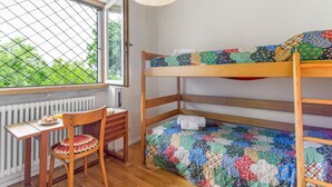 Una cama litera con colcha colorida, un escritorio de madera con silla y una ventana con vista a follaje.