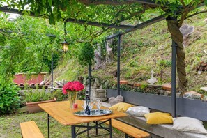 A wooden table with benches, a vase with flowers, and a lantern under a pergola in a garden setting. - GuestHost - Charming and bright flat for 5 people in Cernobbio, in the hamlet of Rovenna, on the way up to mount Bisbino.The apartment, furnished with vintage and modern furniture, comes with private parking and enjoyable outdoor spaces, like the pergola (Cernobbio)