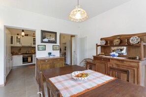 A kitchen with wooden cabinets, a dining table with a placemat, and a hanging light fixture. - GuestHost - Charming and bright flat for 5 people in Cernobbio, in the hamlet of Rovenna, on the way up to mount Bisbino.The apartment, furnished with vintage and modern furniture, comes with private parking and enjoyable outdoor spaces, like the pergola (Cernobbio)