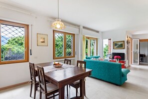 A dining area with a wooden table and chairs, a teal sofa, and a television in the background.
