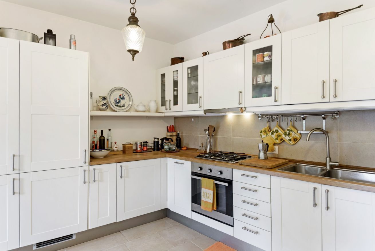 Una cucina con mobili bianchi, un fornello, un lavandino e un espositore a sospensione per pentole.