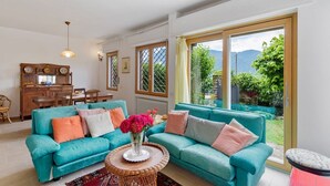 Una sala de estar con sofás color turquesa, una mesa de comedor de madera y vistas a zonas verdes y montañas a través de grandes ventanales.