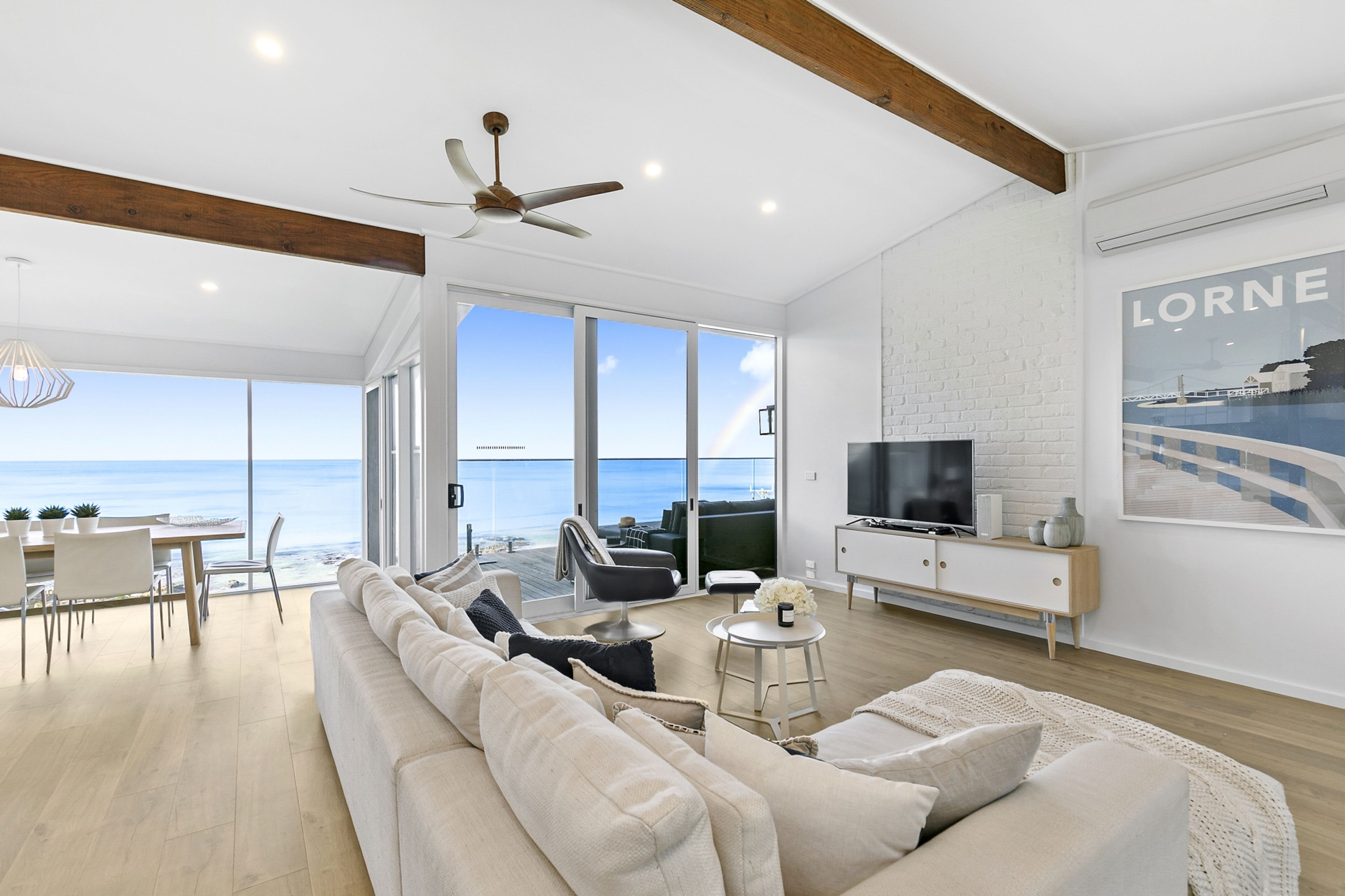 A spacious living room with a large sofa, a television, and a view of the ocean.