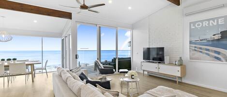 A spacious living room with a large sofa, a television, and a view of the ocean.