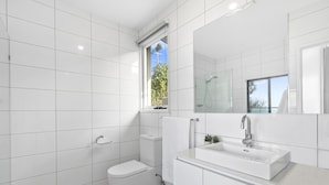 Een moderne badkamer met witte tegels, een toilet, een douche en een wastafel met spiegel.