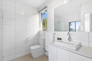 Une salle de bain moderne avec des carreaux blancs, des toilettes, une douche et un lavabo avec un miroir.