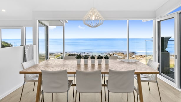 Een eethoek met uitzicht op zee, een houten tafel, vier stoelen en een hanglamp.