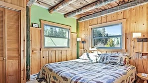 Un dormitorio tipo cabaña de madera con una cama grande, dos ventanas y techo de madera.