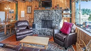 Un interior cálido de cabaña con chimenea de piedra, muebles de cuero y un ventanal con vistas al exterior.
