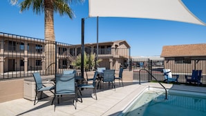 Zona junto a la piscina con mobiliario exterior, una palmera y un edificio con varios balcones.