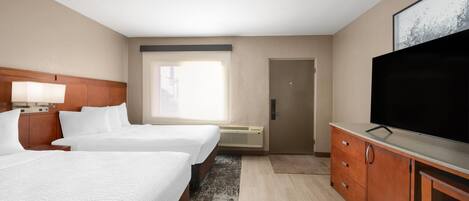 A hotel room with two beds, a TV, a wooden dresser, and a large window.