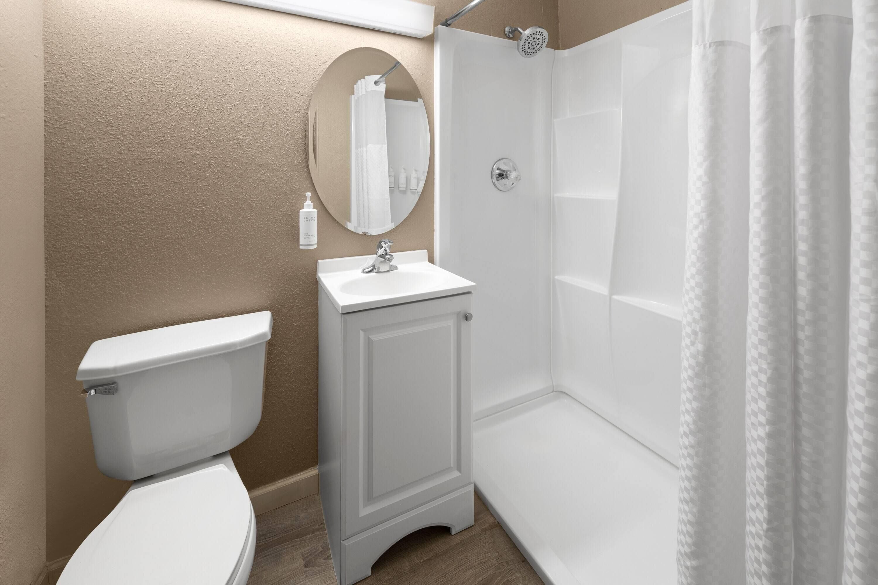 A bathroom with a toilet, sink, mirror, and shower.