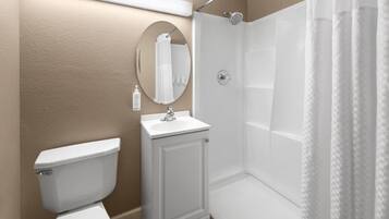 A bathroom with a toilet, sink, mirror, and shower.