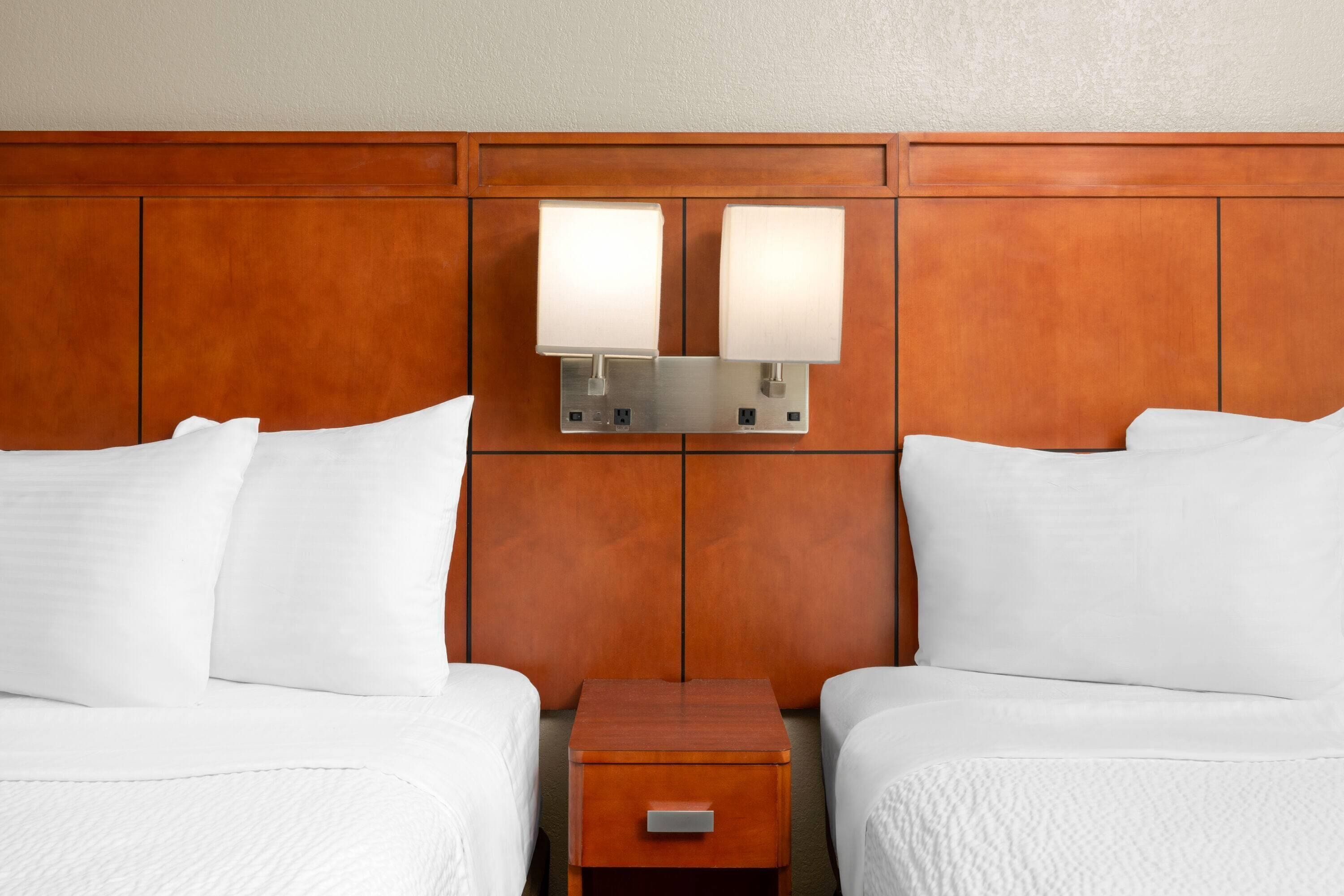 A hotel room with two beds, a wooden headboard, and a nightstand with a lamp.