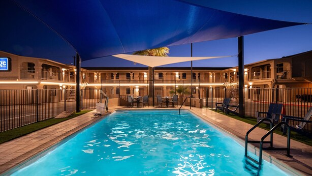 Una piscina con toldo, rodeada por un edificio con varios balcones y zona de estar al aire libre.
