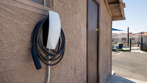 Una estación de carga Tesla fijada a una pared texturizada, con una puerta y una vista de un estacionamiento al fondo.