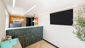 Un área de recepción con diseño moderno, que presenta un panel de pared de madera, una pantalla digital y una pared decorativa de azulejos verdes.
