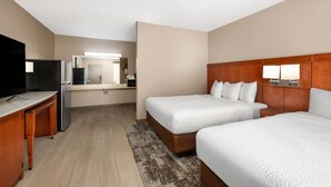 Habitación de hotel con dos camas, un escritorio, un televisor y una kitchenette.