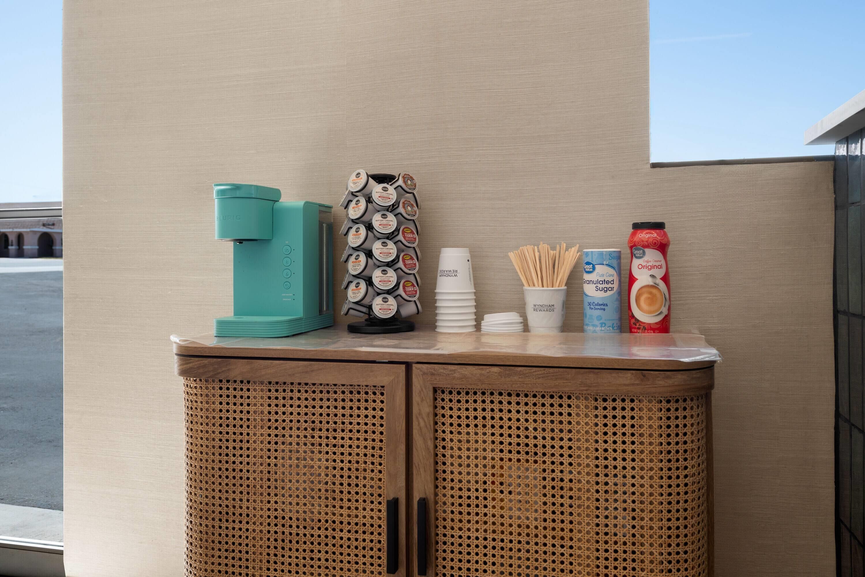 A beverage station with a coffee maker, a thermos, a bottle of soy milk, a cup of coffee, and a bottle of orange juice.