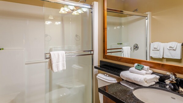 Un baño moderno con cabina de ducha de vidrio, tocador con lavamanos y un espejo grande.